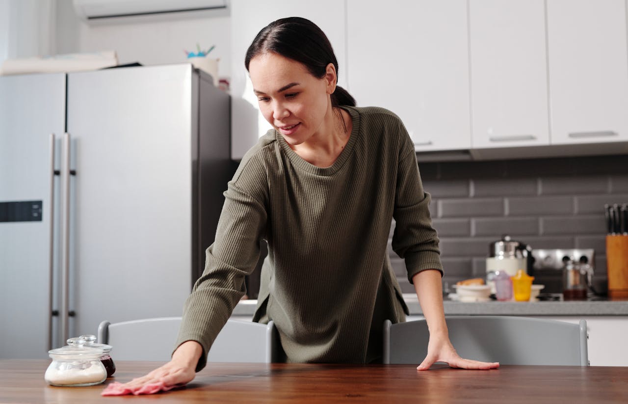 Woman cleaning a kitchen table with a cloth in a modern kitchen setting, maintaining hygiene.